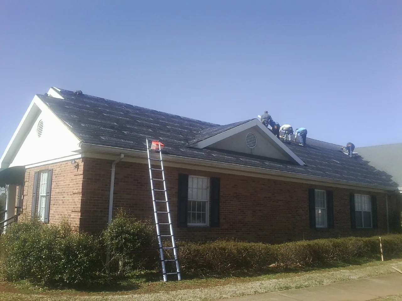 Crew tearing shingles off a brick ranch roof with a ladder set — Metal Roof Repair work by our crew in Arcadia