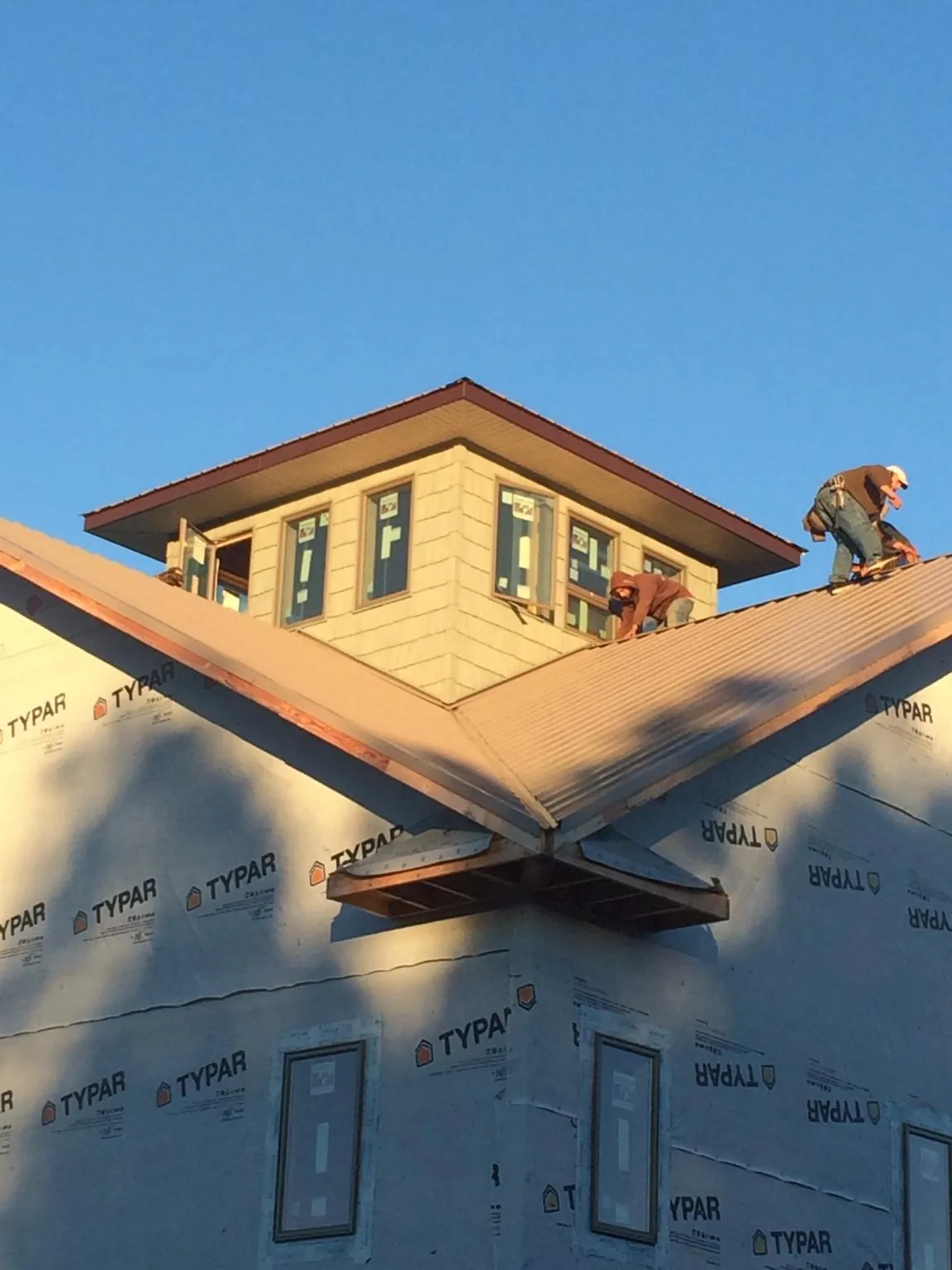 Roofers working around a rooftop cupola on a new metal roof at sunset in Arcadia